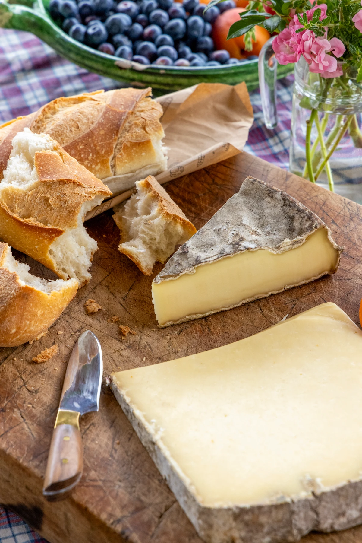 a breakfast spread of cheese, bread, and fruits on a farmhouse table.